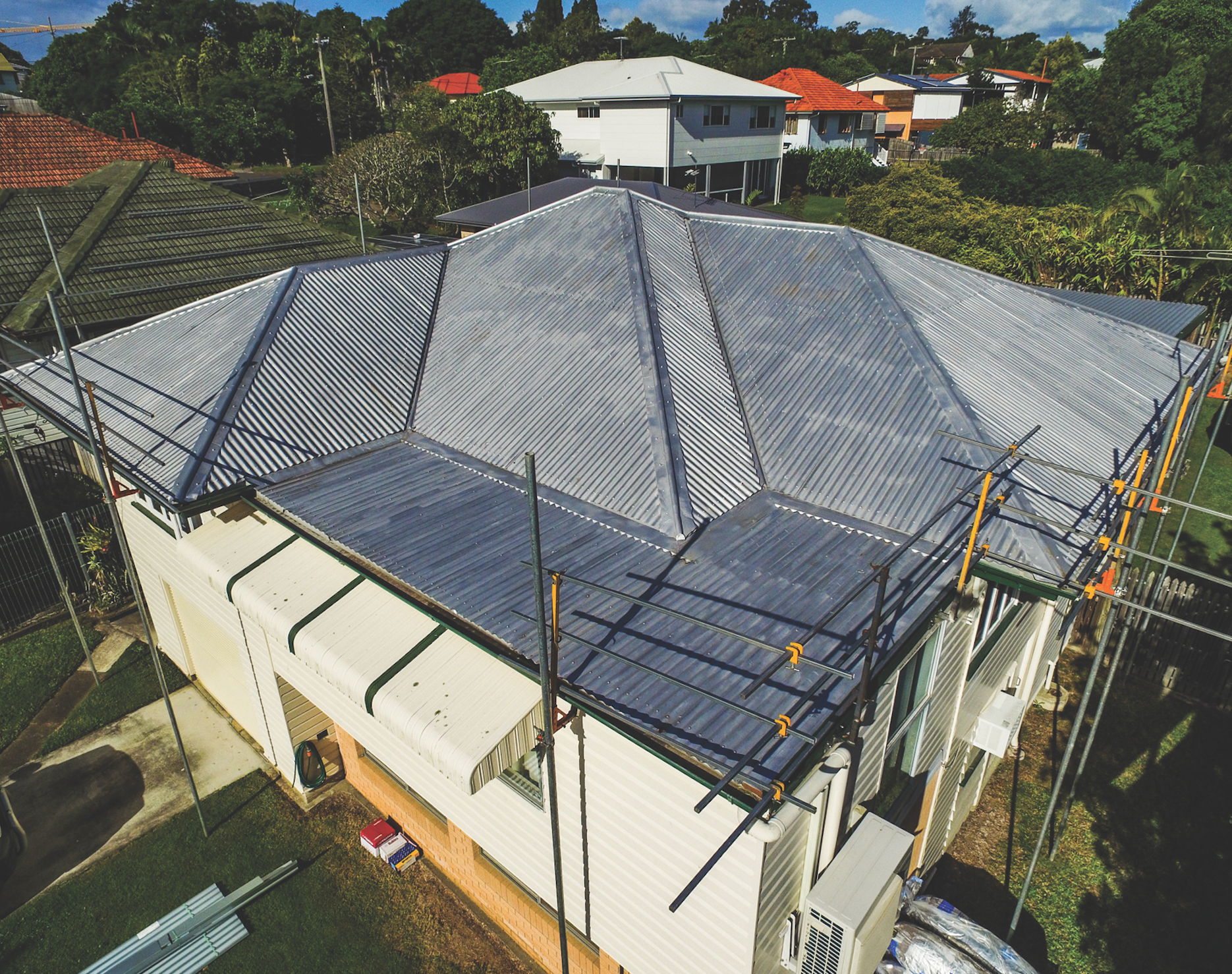 Aerial view of a house with a gray metal roof under construction, surrounded by trees and neighboring homes