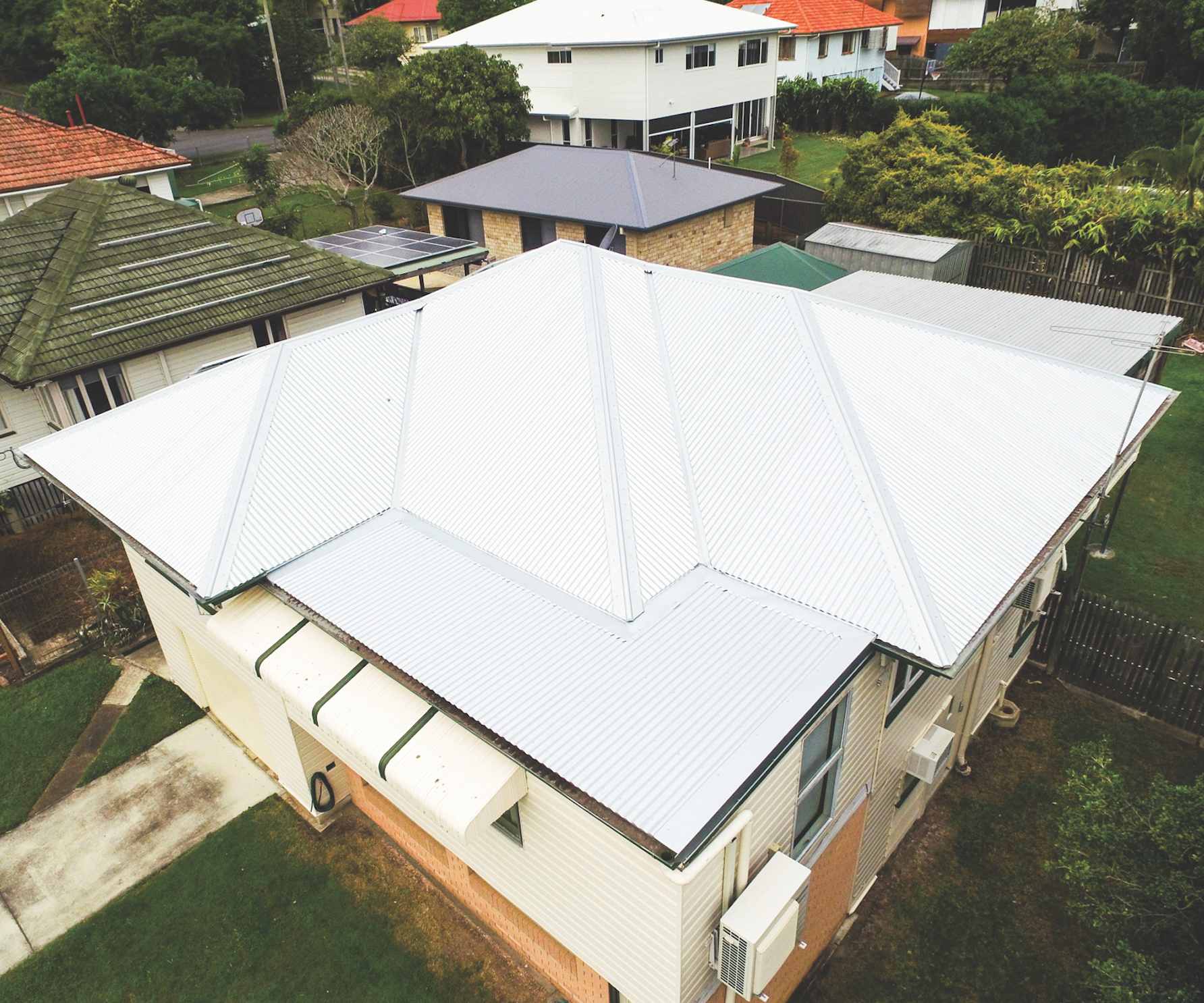 Aerial view of a house with a white metal roof in a green residential area