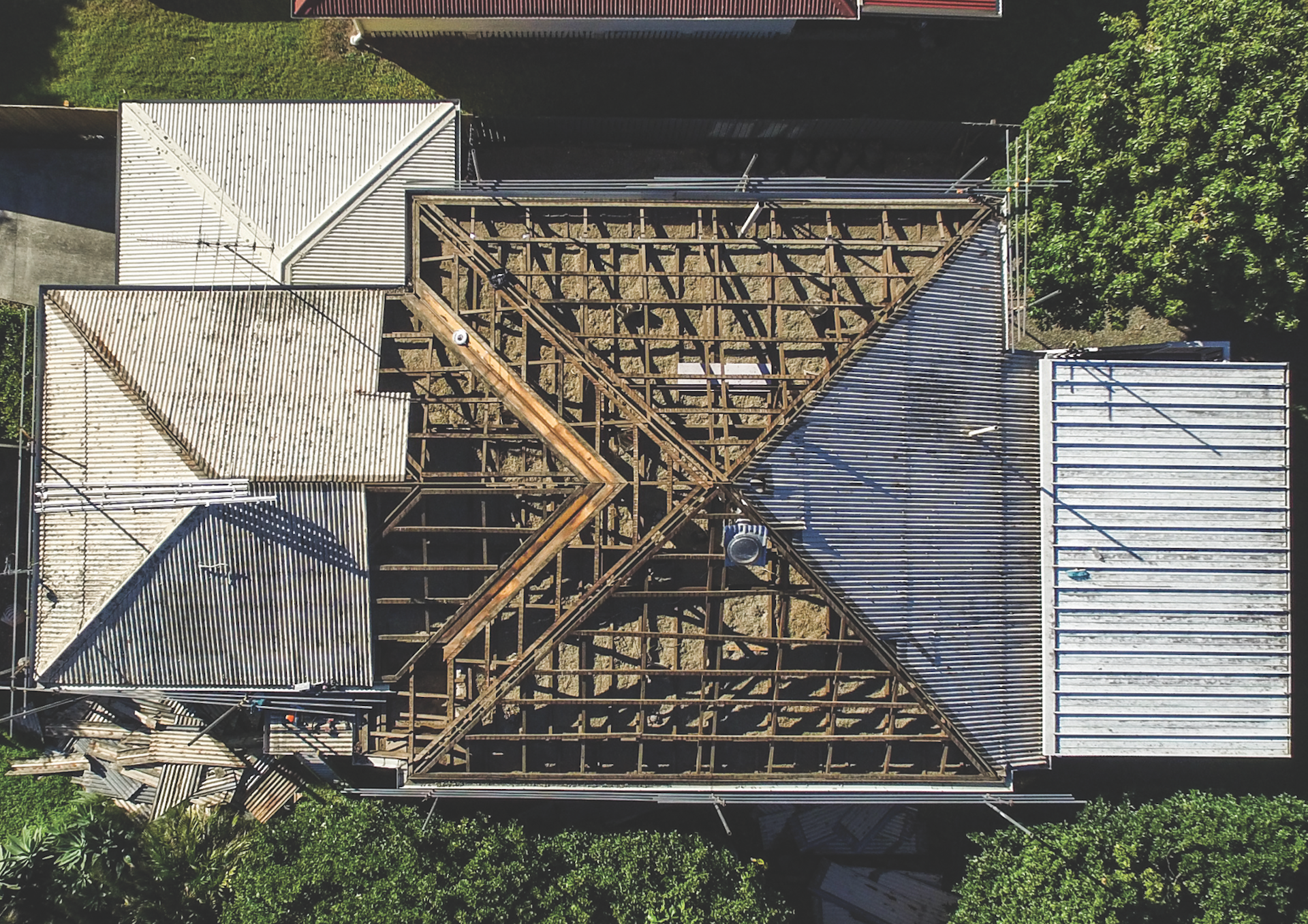 Aerial view of a brown shingled house roof with solar panels and surrounding trees