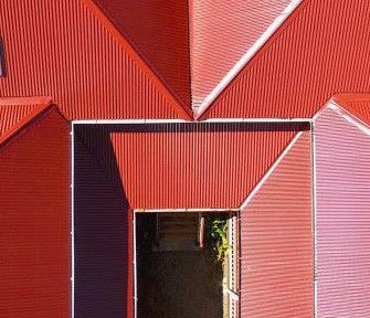 Red corrugated metal facade with a geometric doorway framing a dark entrance