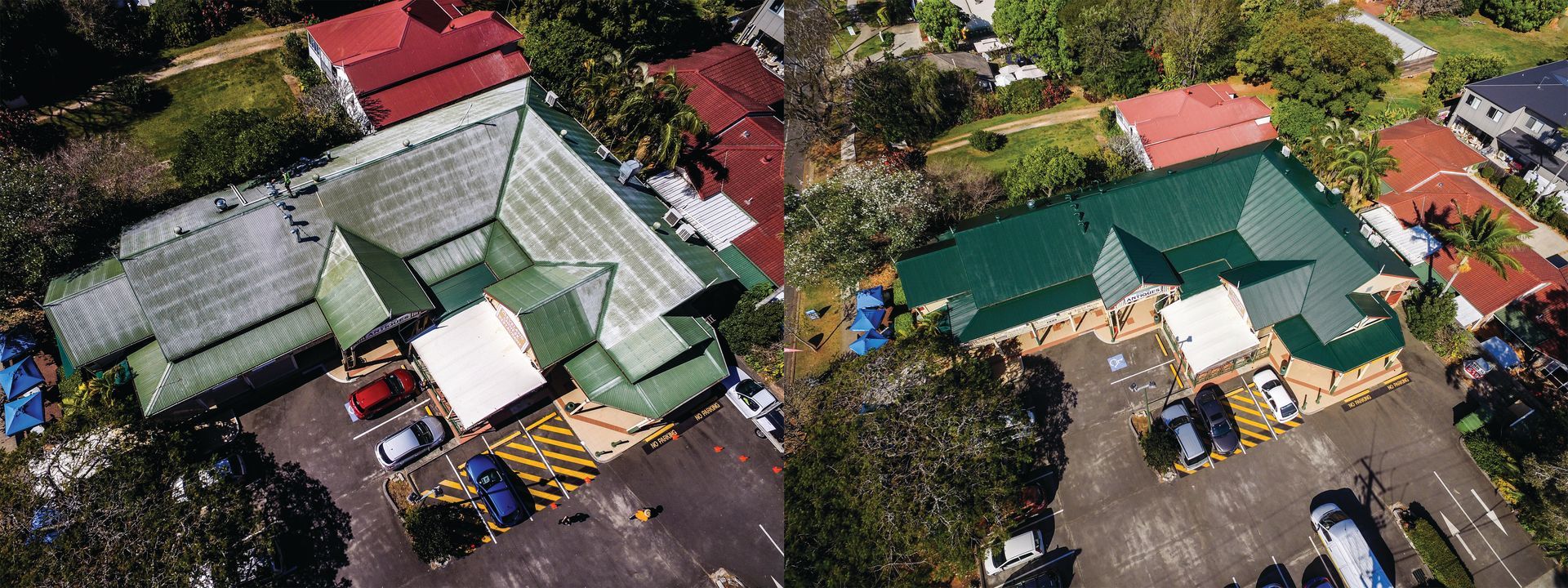 Aerial view of green-roofed buildings and parked vehicles in a paved lot surrounded by trees.