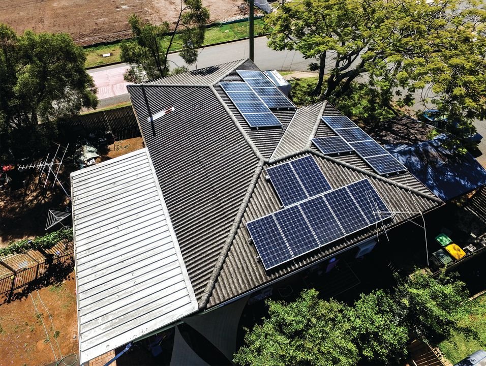 Aerial view of a house roof with multiple solar panels and a white metal awning, surrounded by trees.