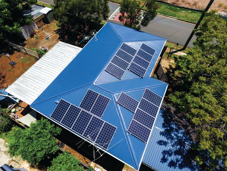Aerial view of a house with a red roof and rooftop solar panels.