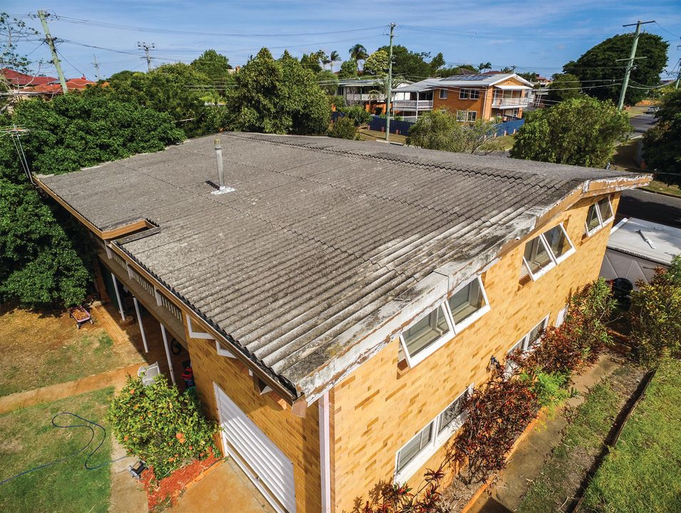 Aerial view of a brown shingled house roof with solar panels and surrounding trees