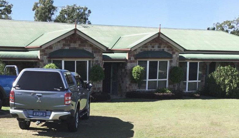 Single-story brick house with a green roof and a dark SUV parked on the lawn in front.