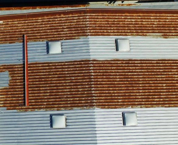 Stacked corrugated metal panels, rust-brown and silver, with small square windows and a red vertical stripe