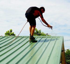 Worker using a rope to clean a green metal roof