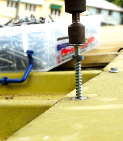 Close-up of a drill fastening a screw into a yellow metal surface.