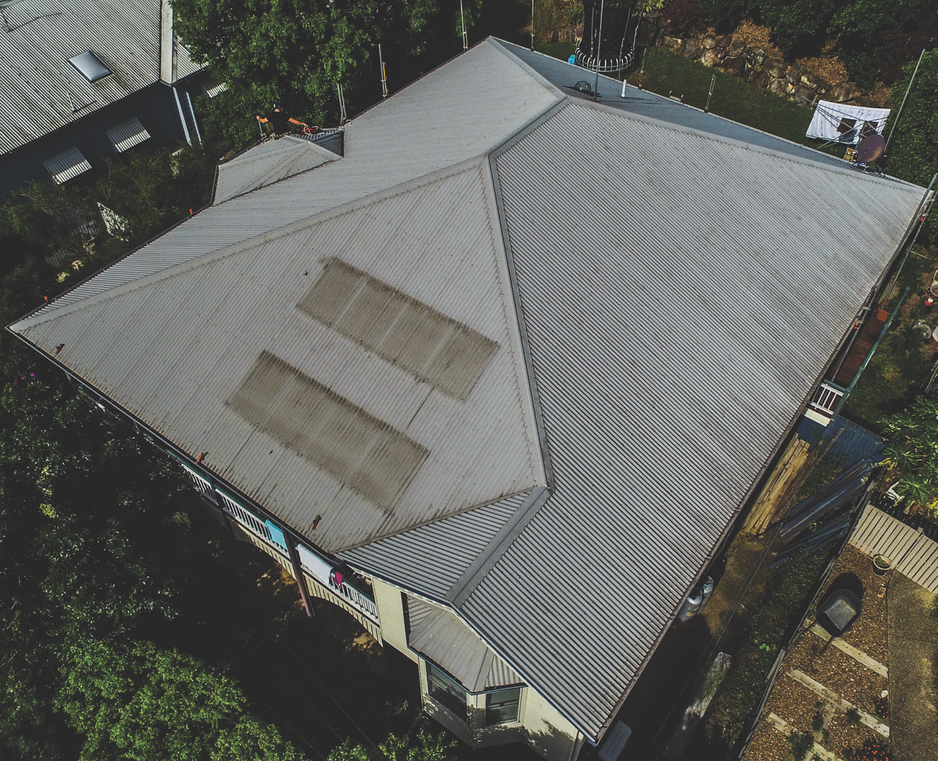 Aerial view of a gray metal-roofed house surrounded by trees and a small yard