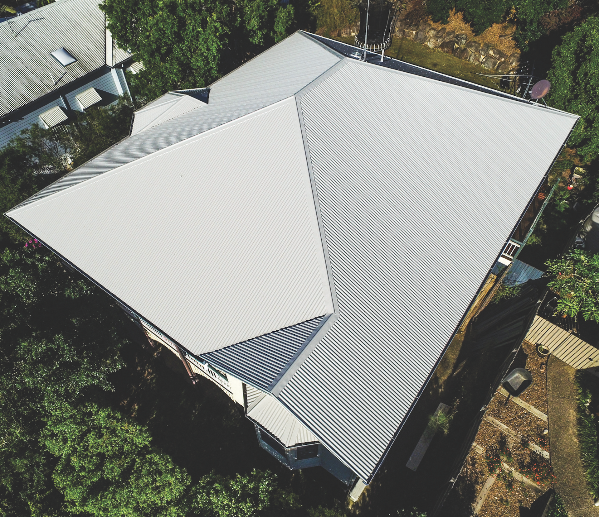 Aerial view of a house with a light gray roof surrounded by trees and yard.