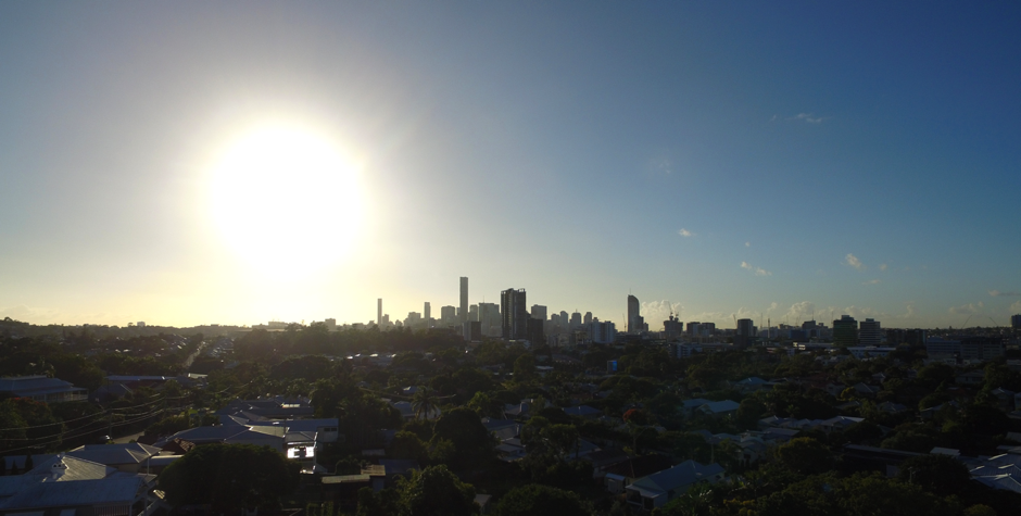 Sunlit city skyline at dusk with bright sun over dark suburban rooftops