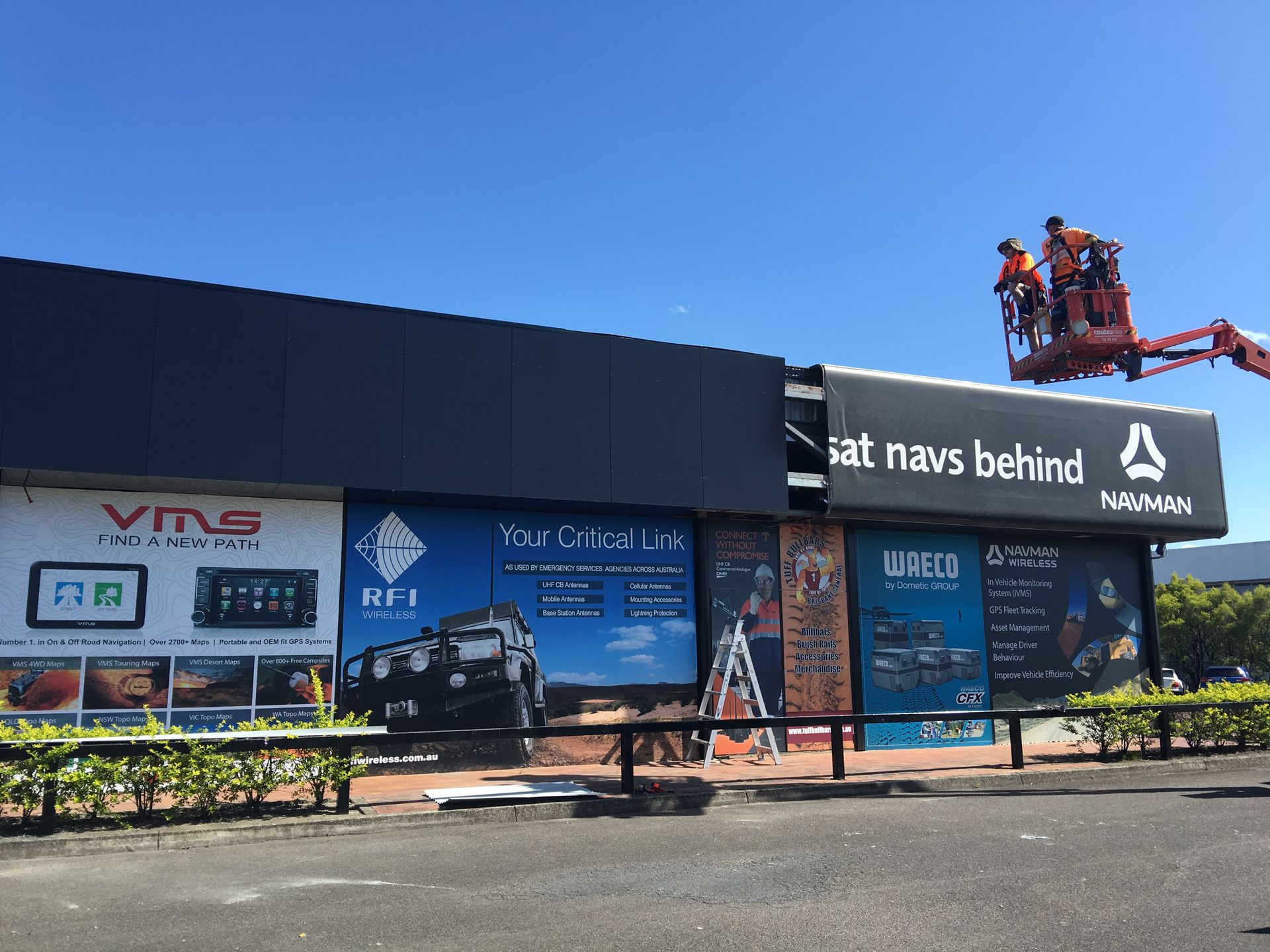 Workers on a roof above a roadside billboard under a clear blue sky