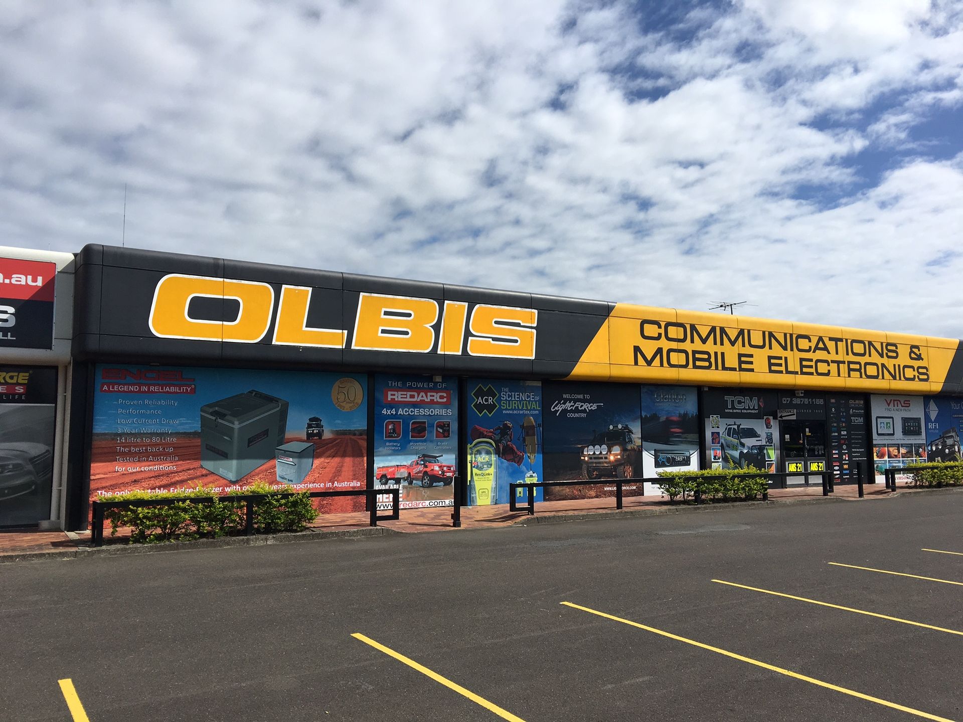 Storefront of OLBIS Communications & Mobile Electronics with yellow sign and storefront windows in a parking lot