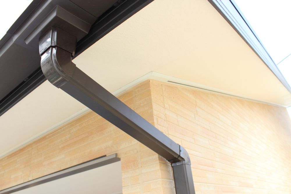 Black metal rain gutter and downspout on a house with cream siding and brick wall