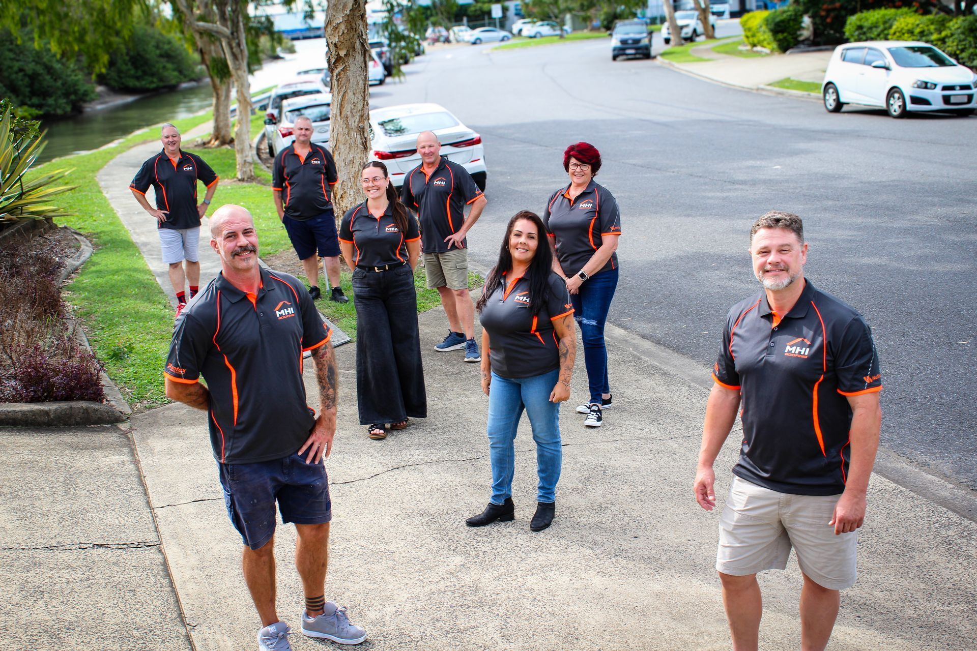 Group of people in black shirts standing and smiling on a suburban street