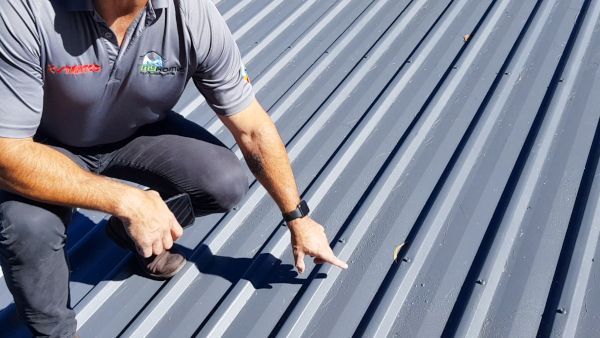 Worker inspecting a gray corrugated metal roof with a hand tool