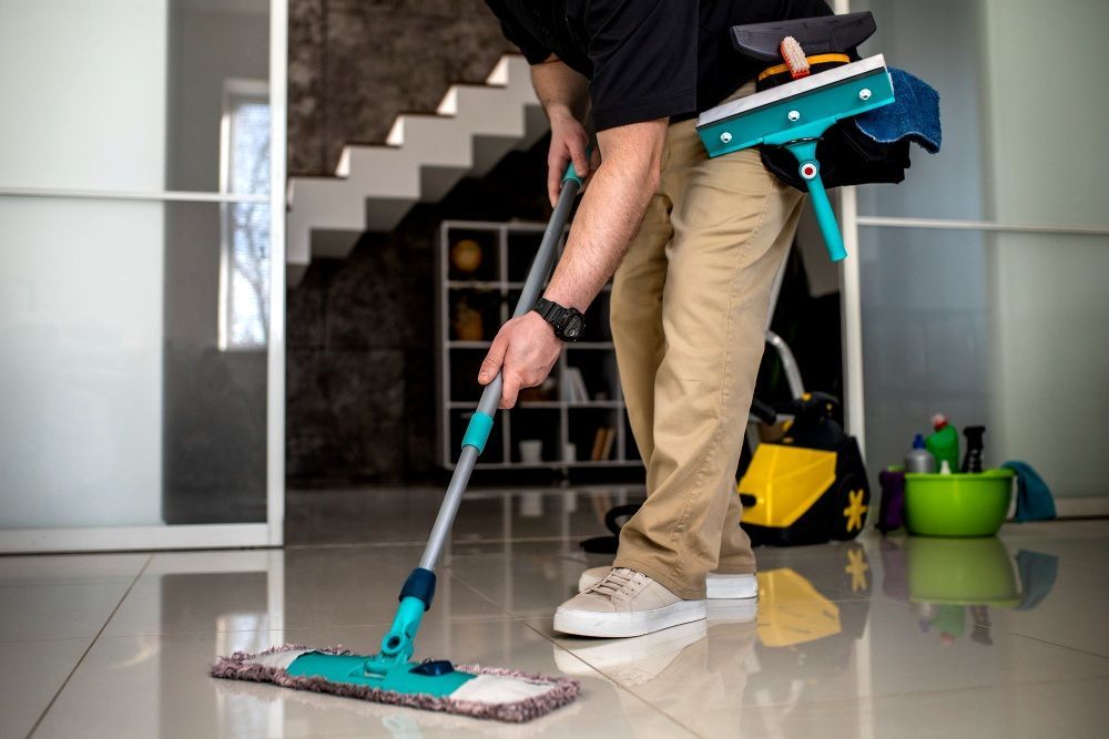 A person mopping a shiny floor in a modern home, with cleaning supplies nearby.