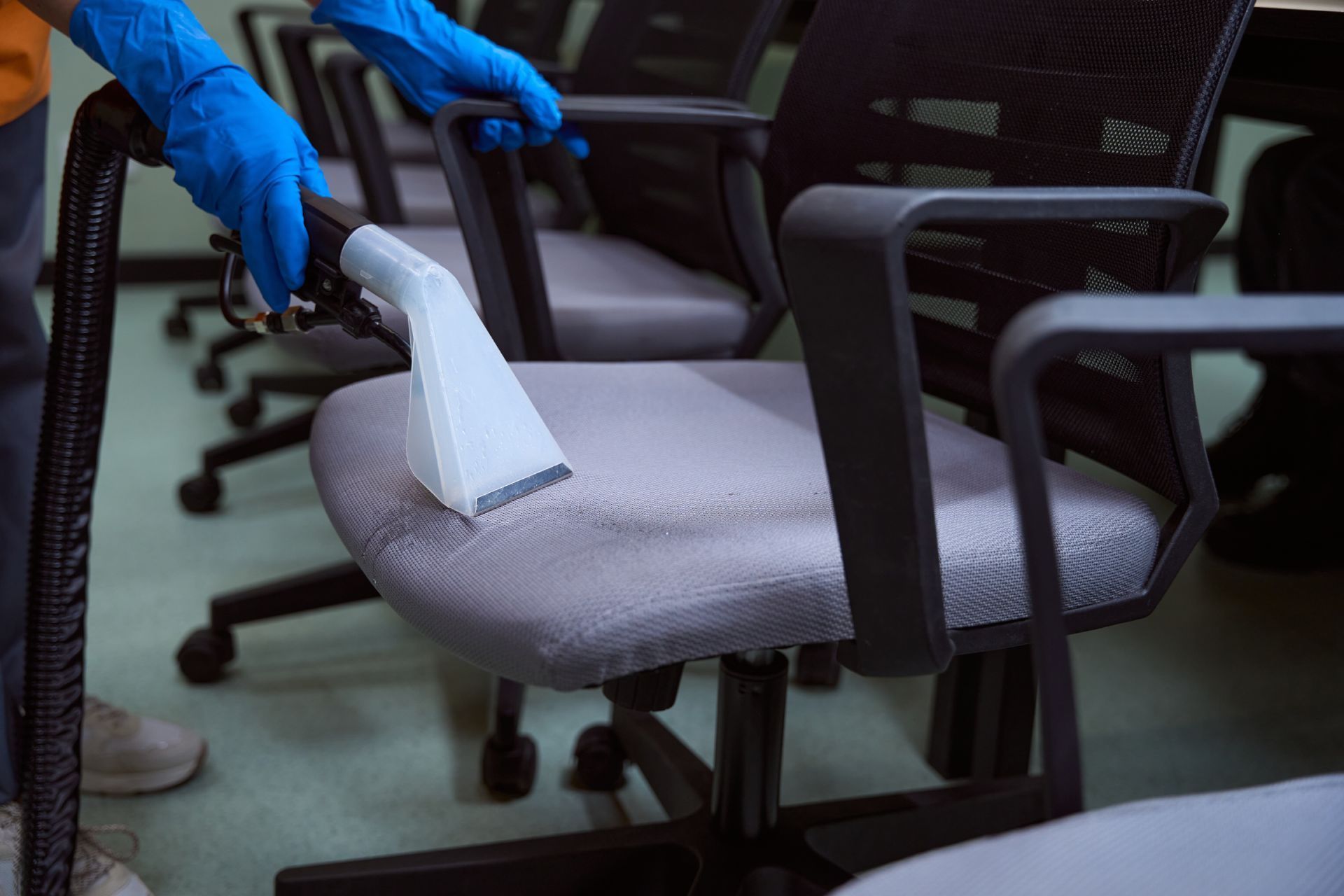 Person wearing gloves vacuuming office chair with cleaning tool.