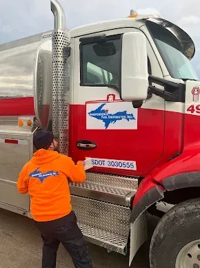 Fuel nozzle dispensing fuel into a vehicle's tank. A gloved hand holds the nozzle.
