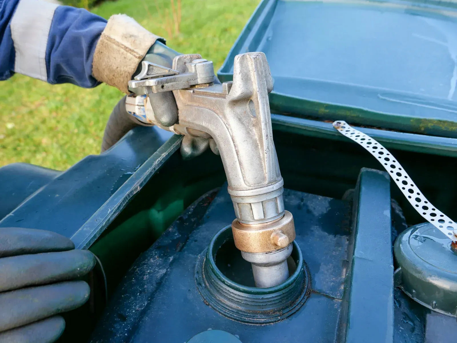 Fuel nozzle dispensing fuel into a vehicle's tank. A gloved hand holds the nozzle.