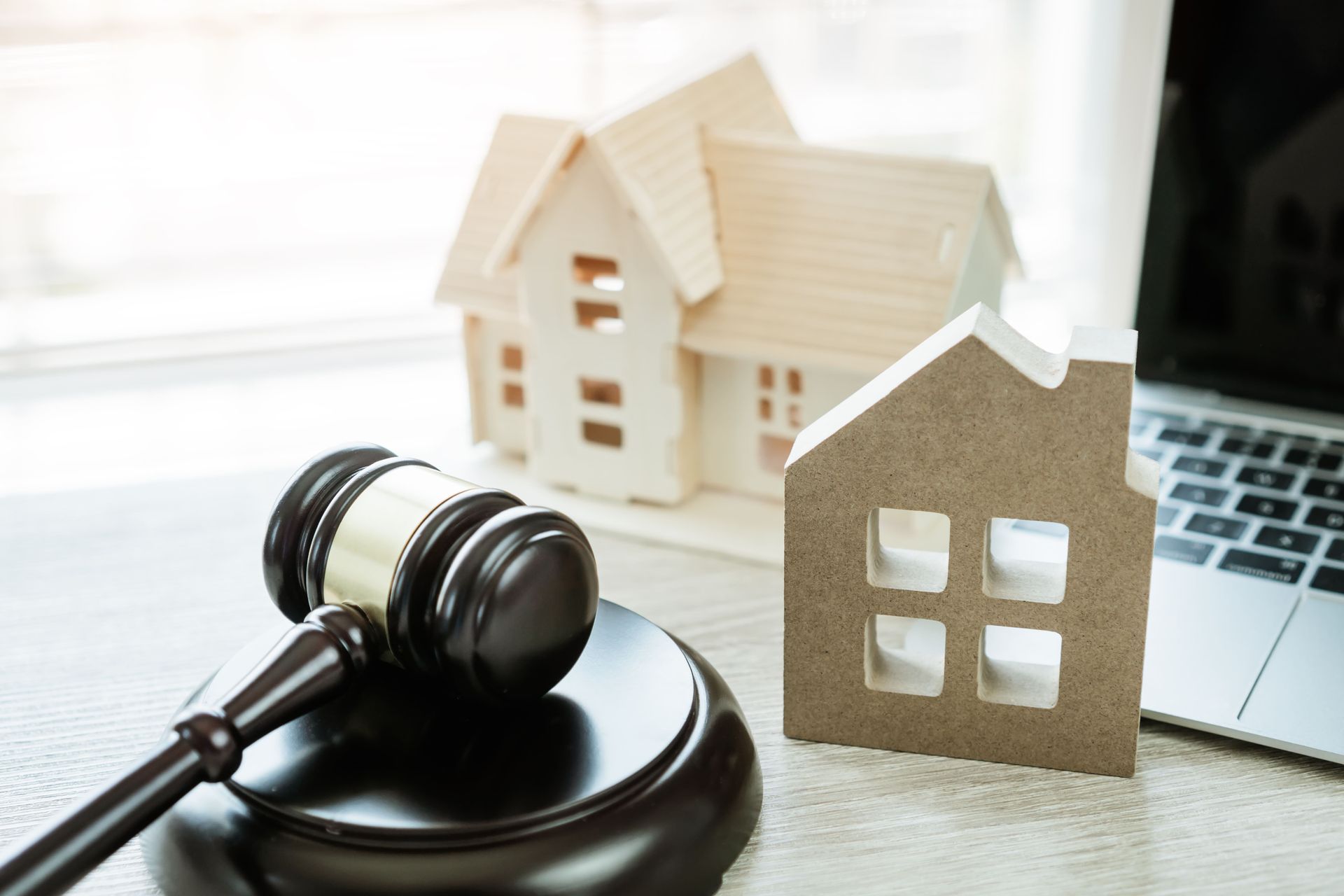 Gavel, model houses, and laptop on a desk, possibly representing a real estate auction or legal matter.
