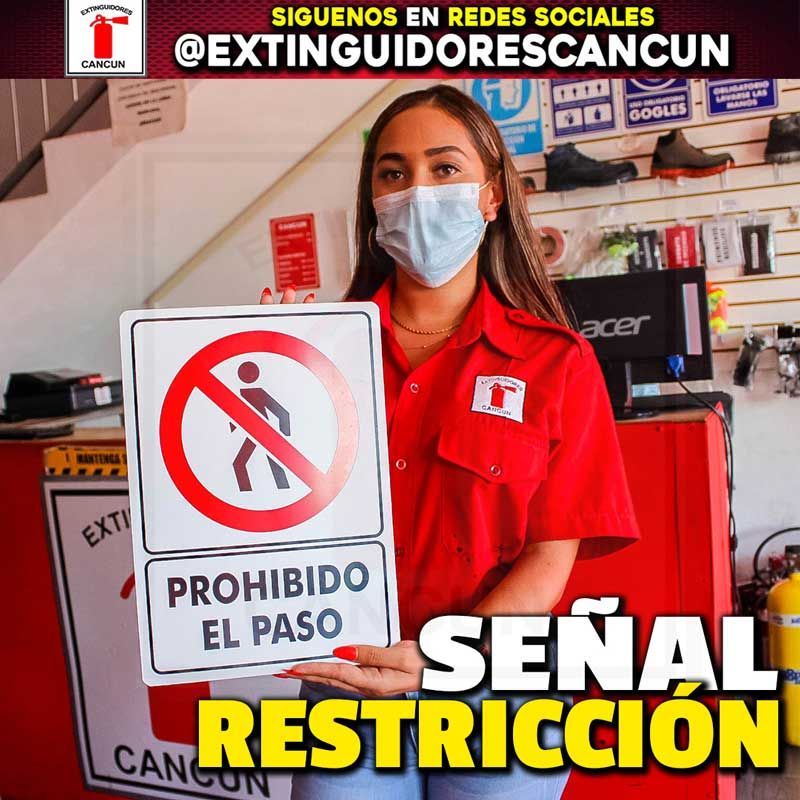 Una mujer con máscara sostiene un cartel que dice prohibido el paso.