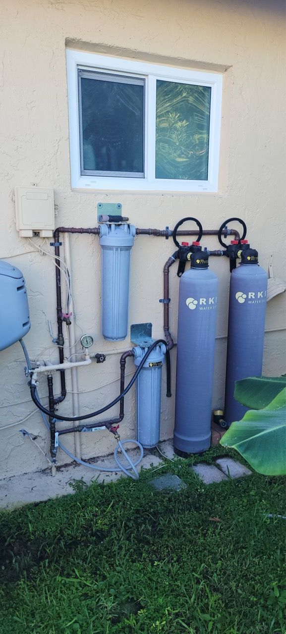 Outdoor water filtration system with blue tanks and pipes beside a house window and grass.
