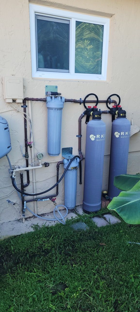 Outdoor water filtration system with two blue tanks and a gray filter beside a house wall and window