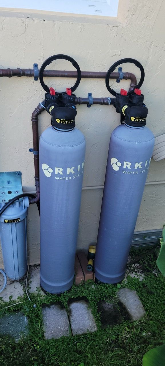 Two blue water softener tanks with black control heads beside a beige wall outdoors