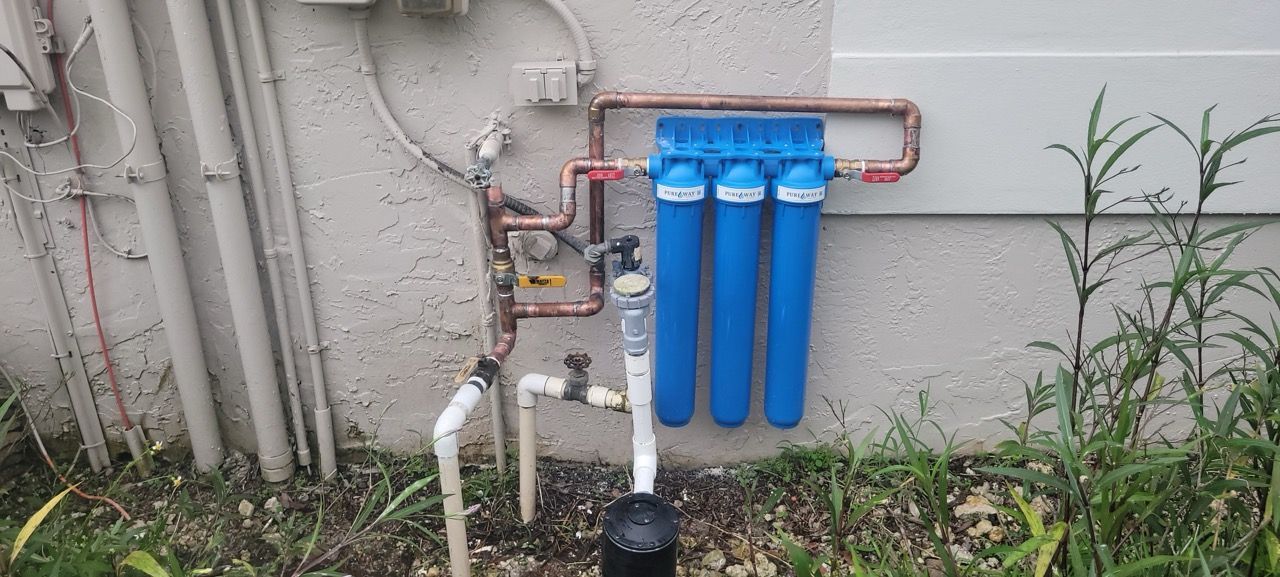 Blue water filtration system mounted on an exterior wall with pipes and grass below