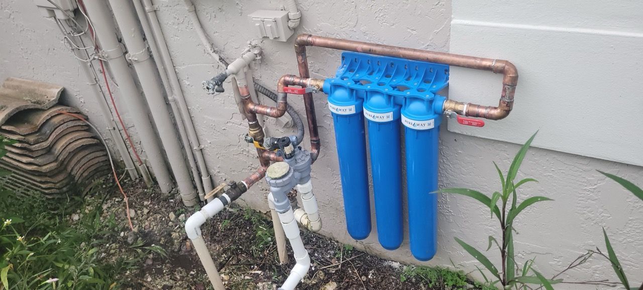 Blue water filter system mounted beside outdoor plumbing pipes and a wall