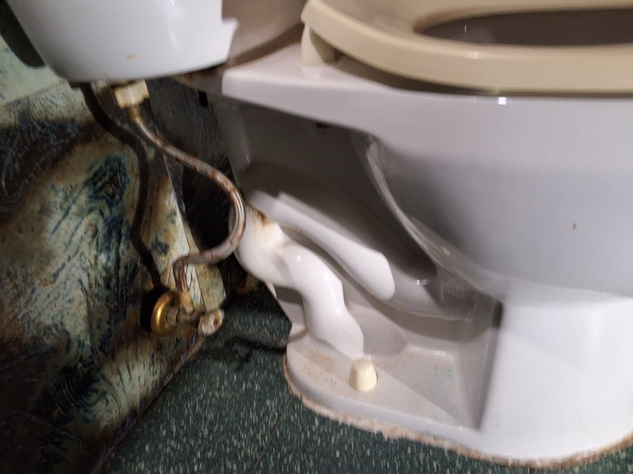 Damaged toilet base with exposed plumbing and water stains beside a wall and floor.