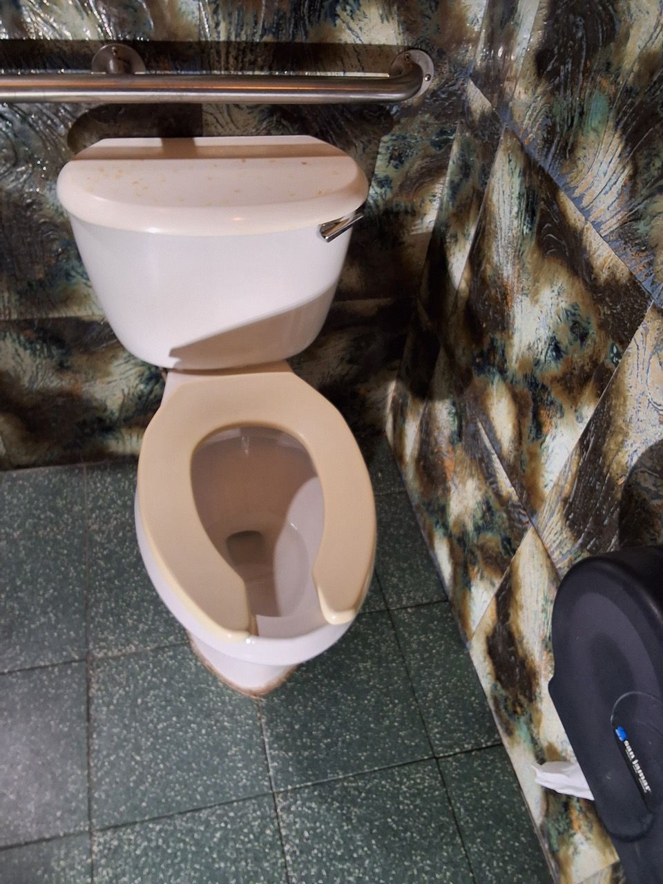 Toilet with the lid up in a small restroom with green tile floor and patterned walls