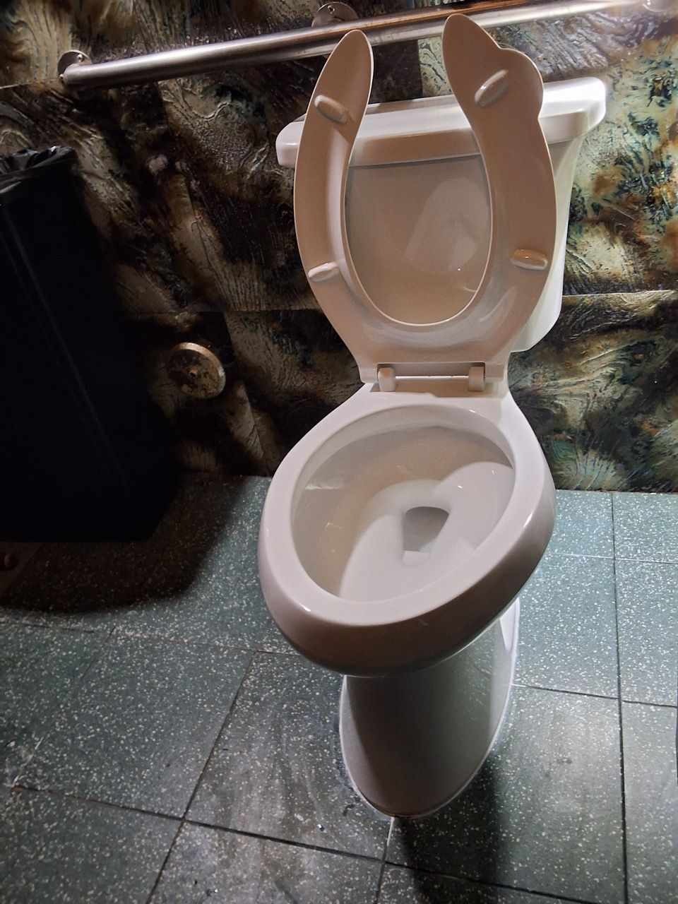 Open toilet with lifted seat in a tiled bathroom, with a grab bar behind it.