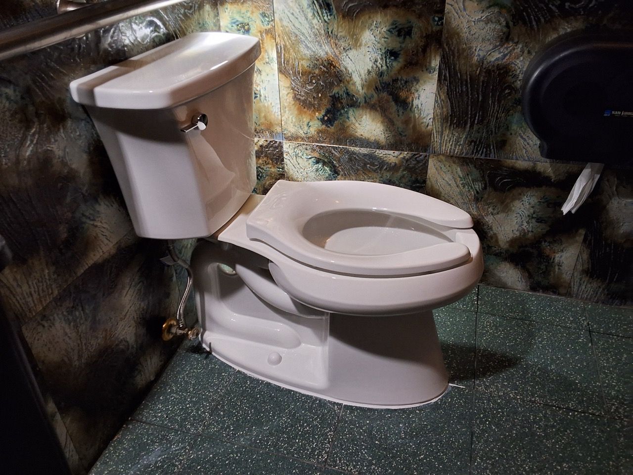 White toilet in a small bathroom with a green speckled floor and marbled walls