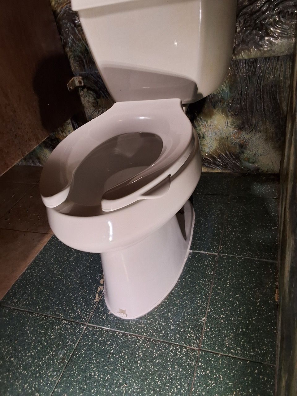 White toilet with open lid in a small bathroom with green speckled flooring.