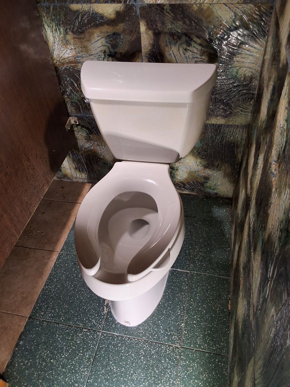 Toilet with a broken seat in a small bathroom, with reflective foil on the wall.