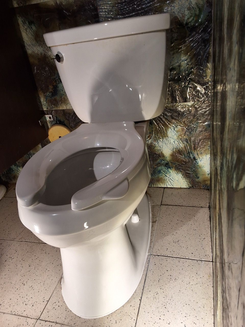 Toilet in a restroom with a raised seat and gray safety rails