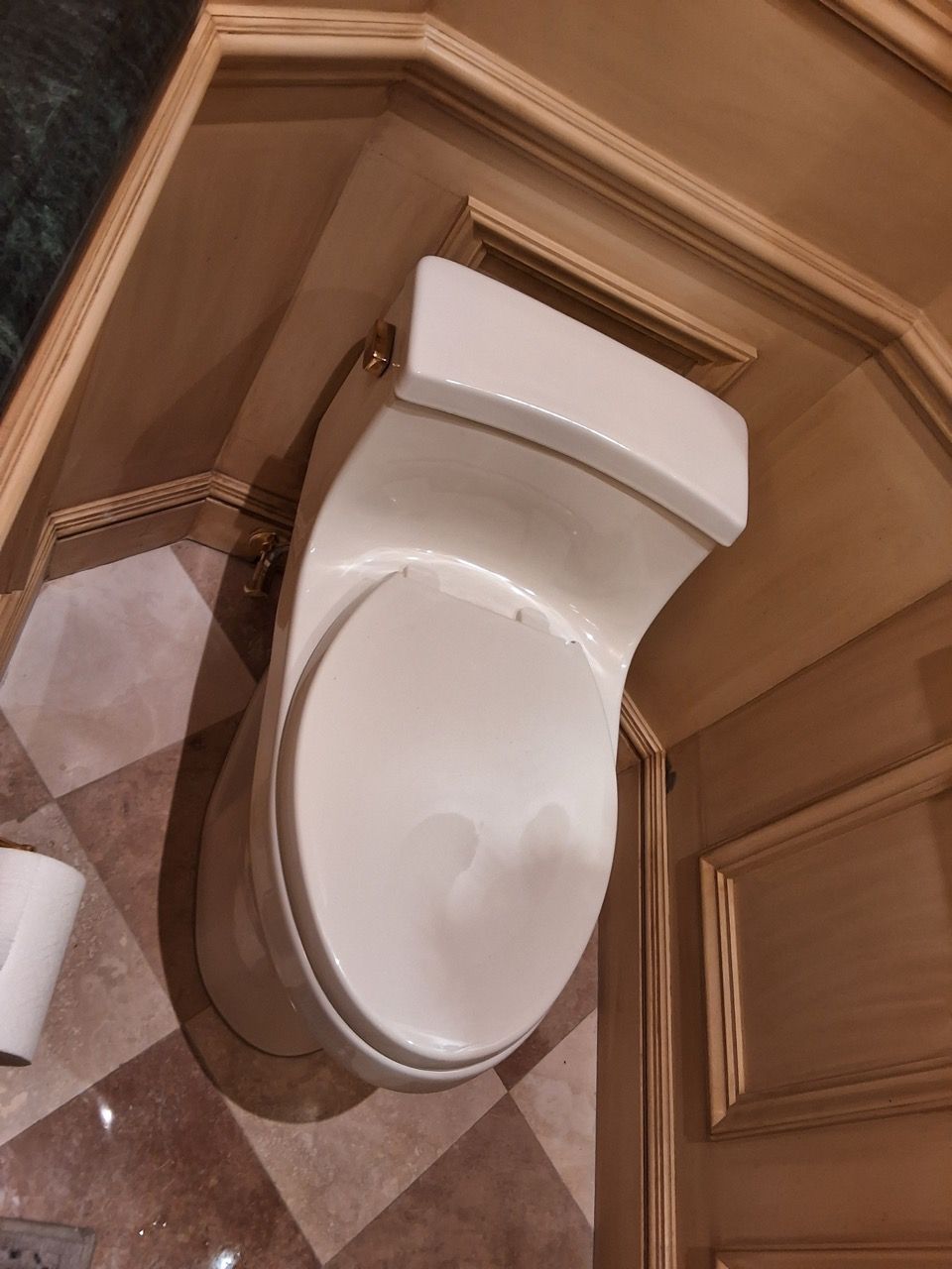 White modern toilet in a tan-tiled bathroom, viewed from above.