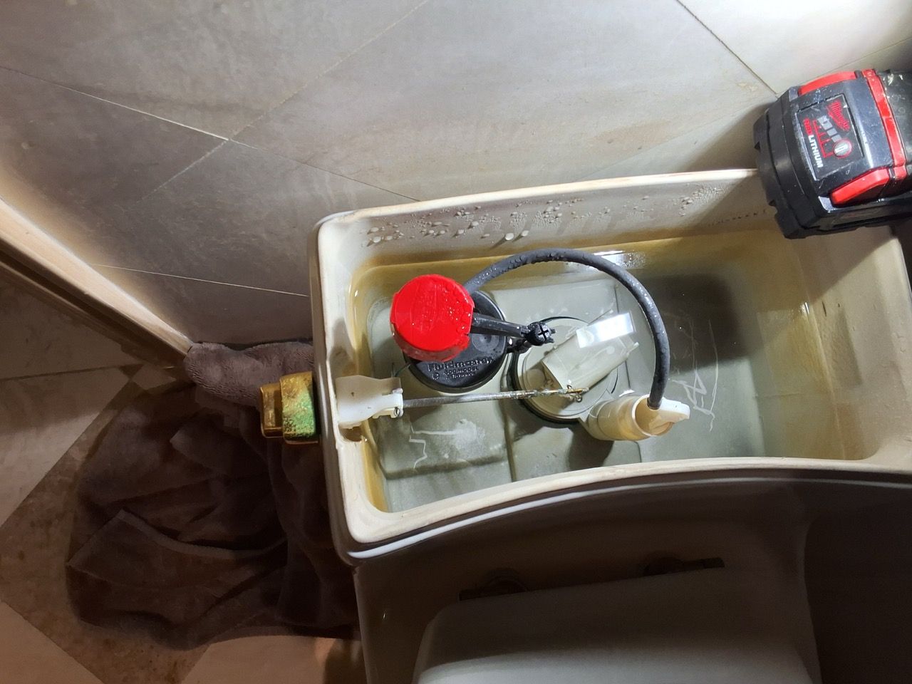 Open toilet tank with red float valve and connected plumbing inside a bathroom.