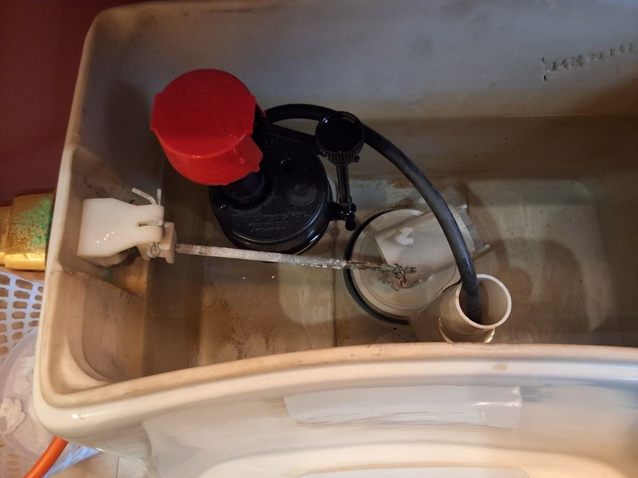Inside a toilet tank, a red-capped fill valve and black hose sit beside the flush mechanism.