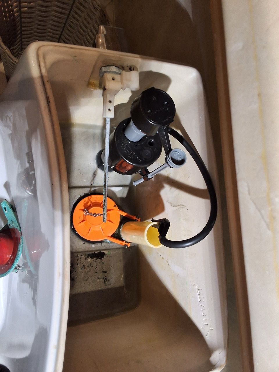 Toilet tank interior with black and orange flush valve components and water fill mechanism.