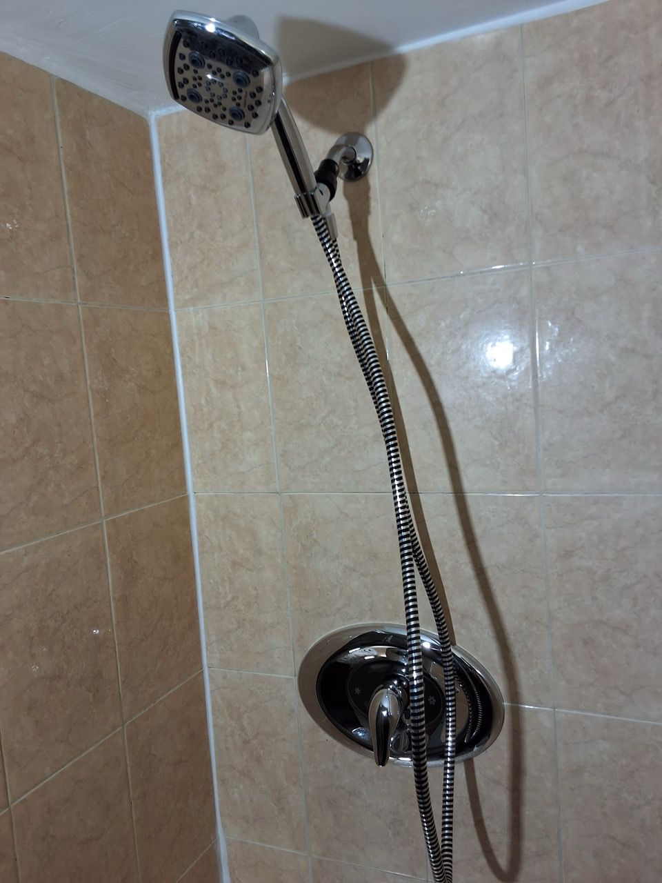 Chrome handheld shower head with hose mounted on beige tiled bathroom wall