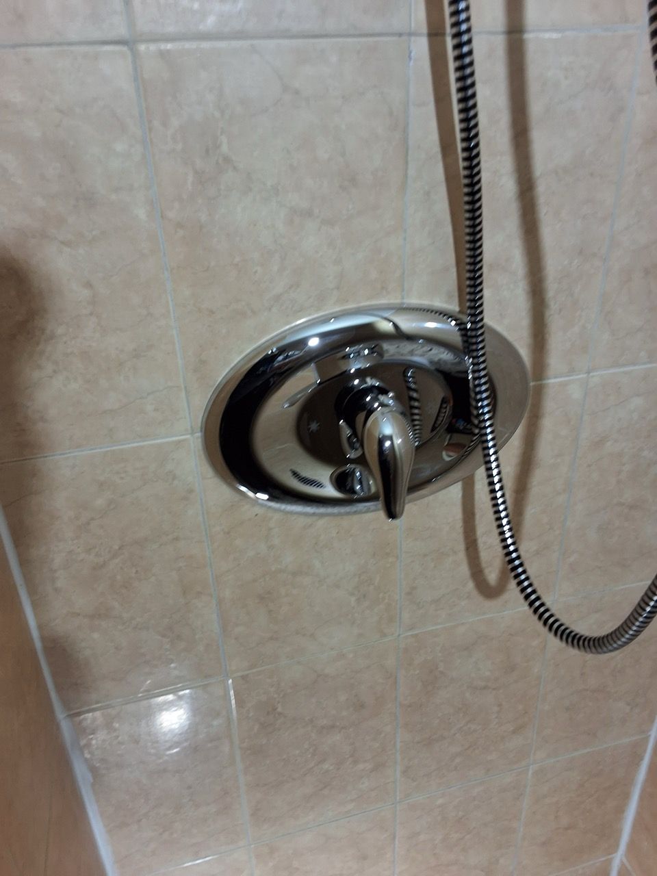 Chrome shower control handle and hose mounted on beige tiled bathroom wall