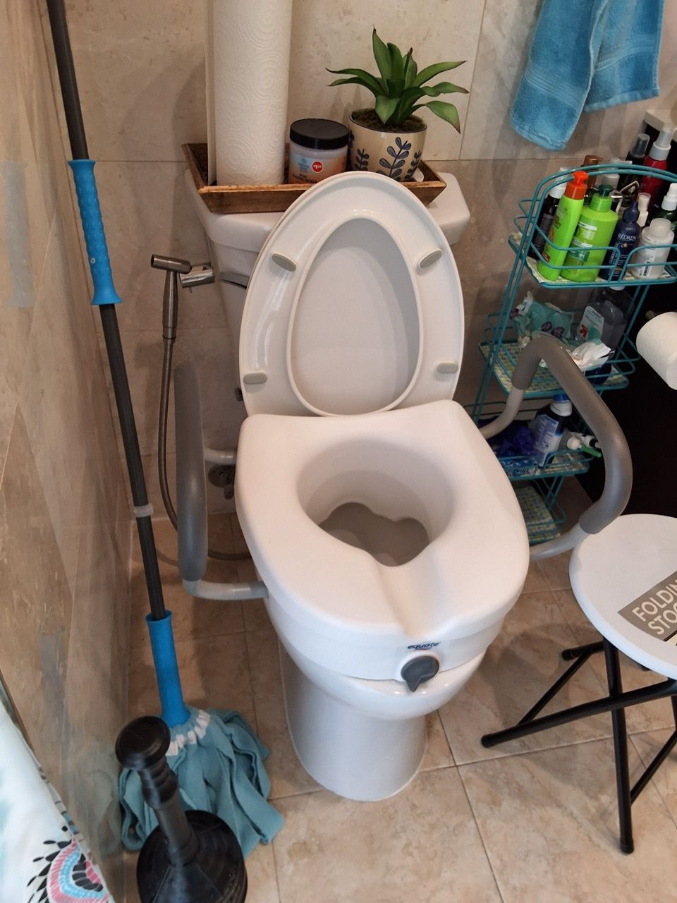 Bathroom with an open toilet, blue mop, and a small shelf of toiletries beside it.