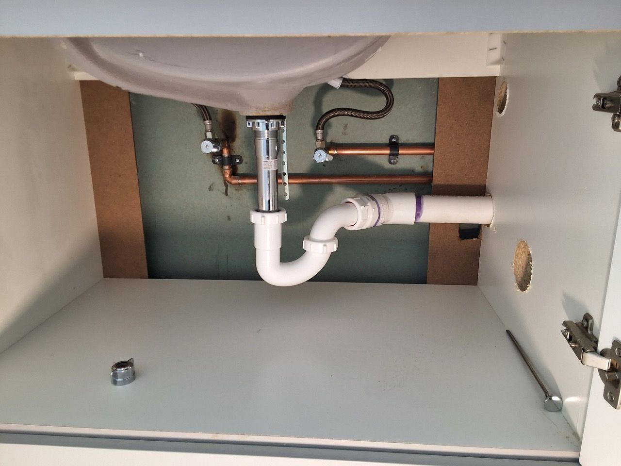 Under-sink cabinet with white plumbing pipes and exposed copper water lines.