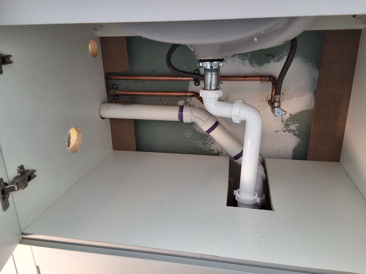 Under-sink cabinet with exposed white plumbing pipes and open access panels