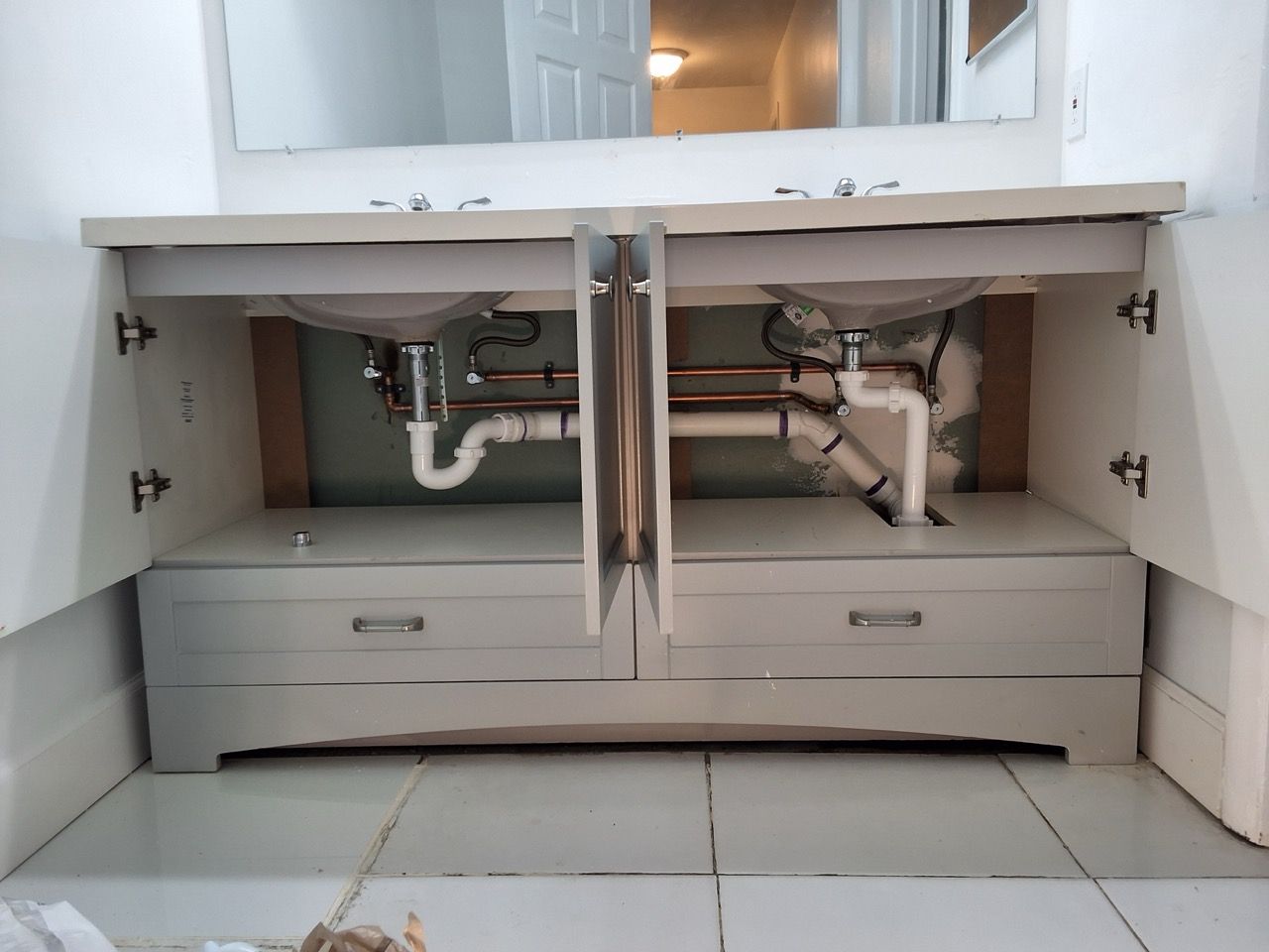 Open bathroom vanity with two drawers, exposed plumbing, and a large mirror above.