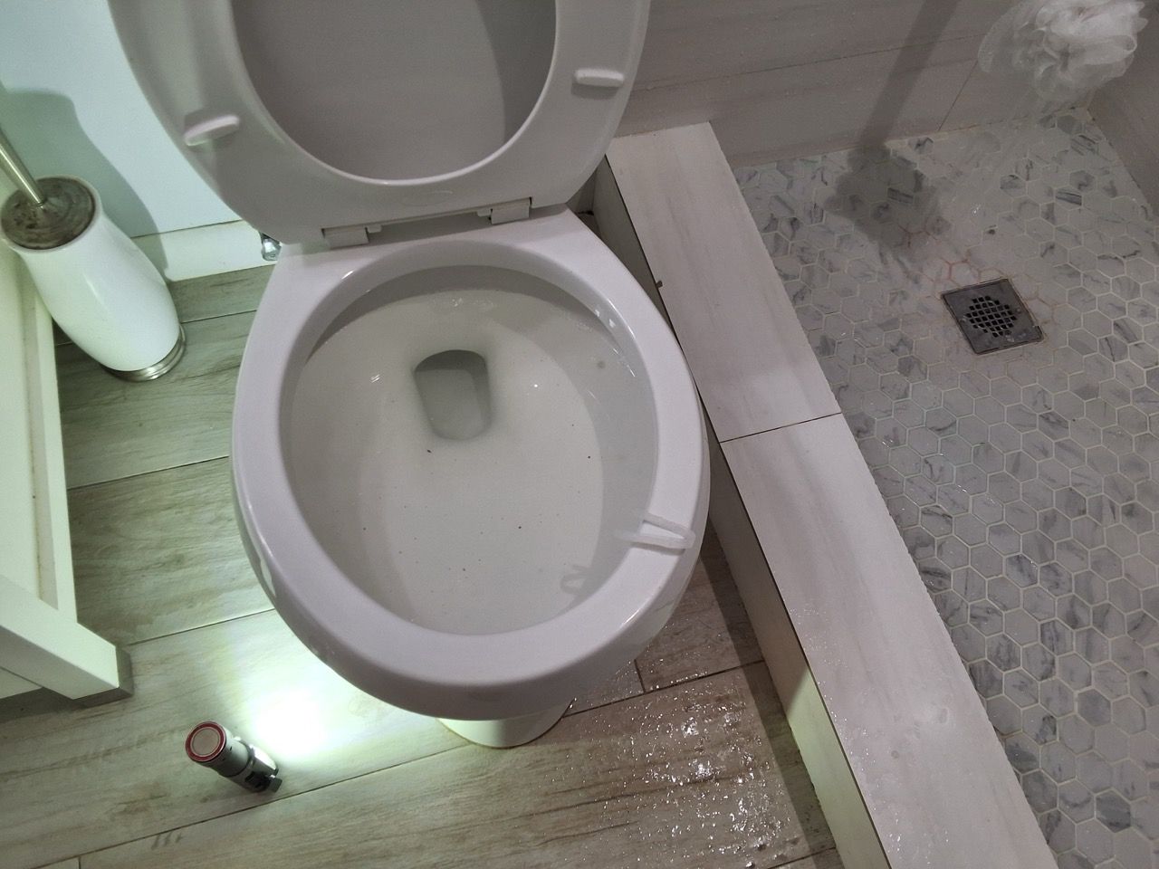 An open toilet in a bathroom with a tiled floor and shower area nearby.