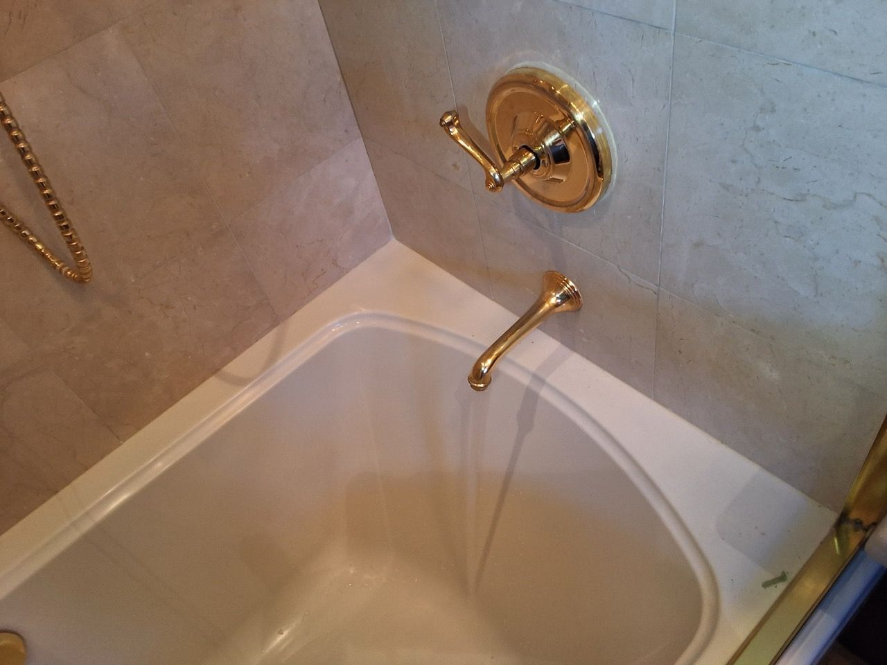 Gold bathtub faucet in a tiled bathroom over an empty tub